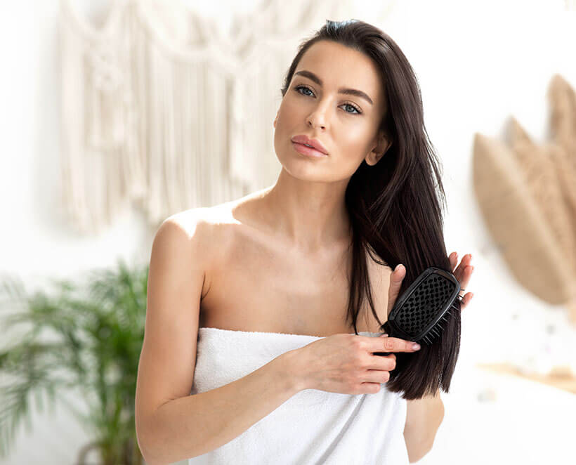 Brunette woman in a white towel brushing her full head of hair