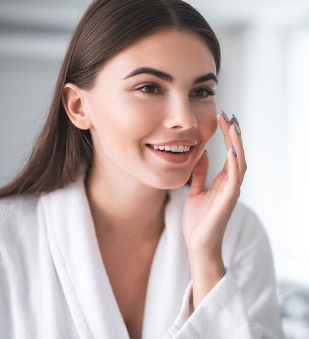 Woman in a white robe admiring her facial skin rejuvenation